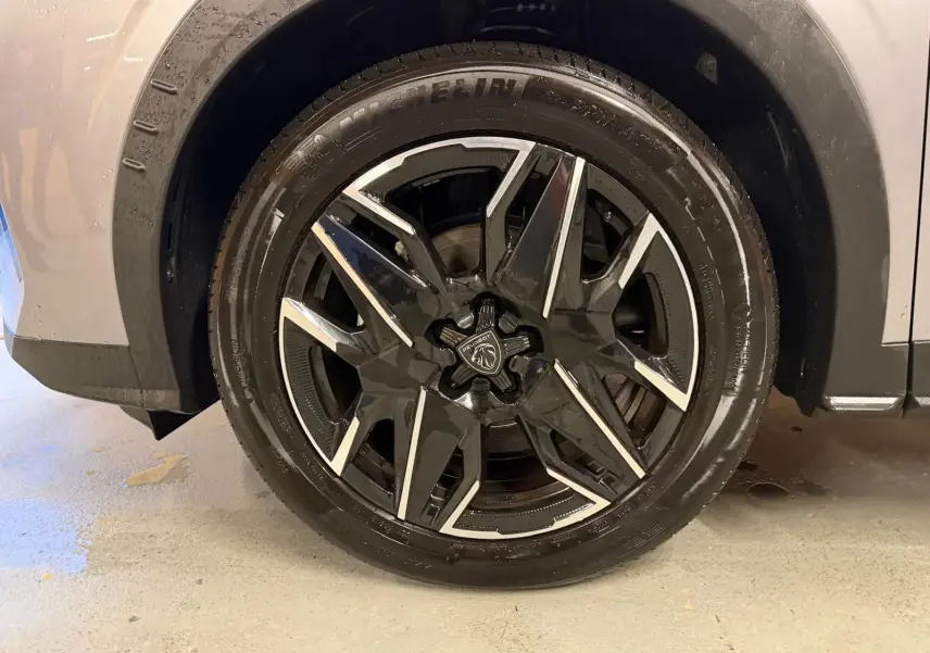 Gros plan sur la roue avant droite du Peugeot 3008 gris 1.2 Hybrid 136 avec jante noire et argentée au design moderne.