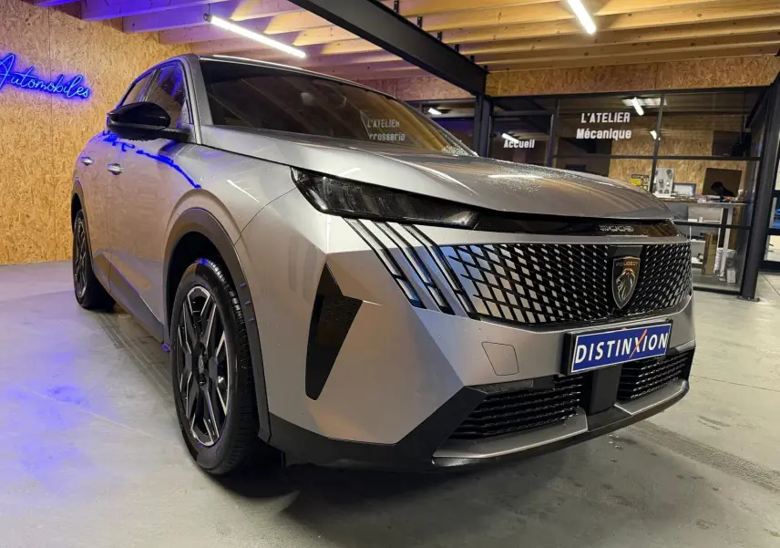 Vue 3/4 avant droit d'un Peugeot 3008 gris 2025 avec calandre noire et signature lumineuse distinctive en intérieur d'atelier.