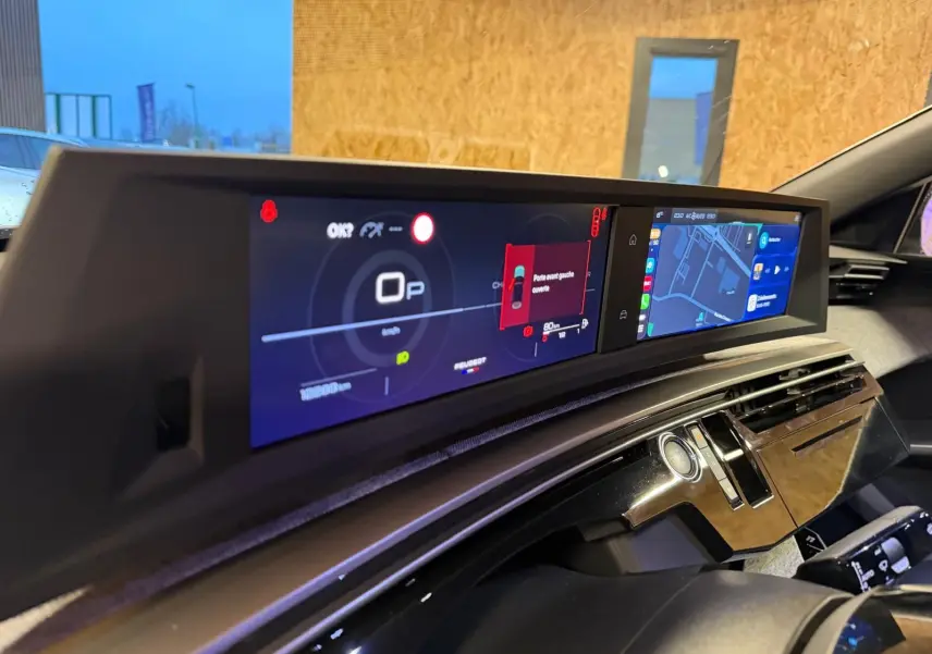 Vue rapprochée du tableau de bord numérique et écran central du Peugeot 3008 gris, affichant la navigation et alertes.