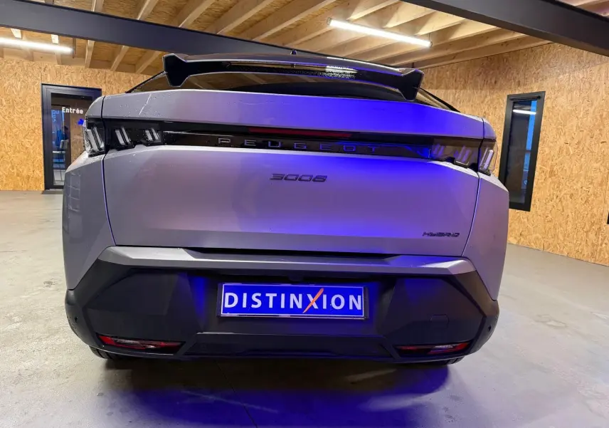 Vue arrière d'un Peugeot 3008 gris hybride 2025 avec signature lumineuse distinctive et toit noir dans un garage.
