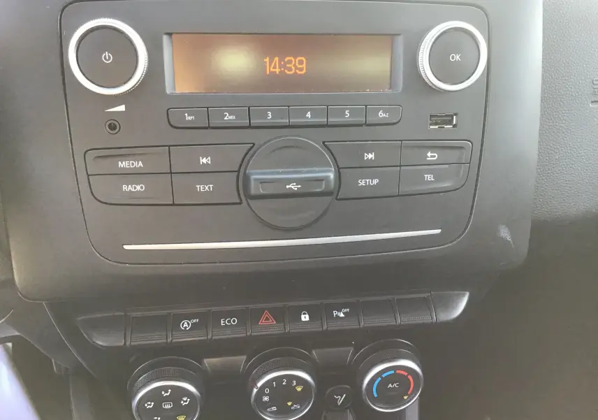 Vue rapprochée du tableau de bord noir du Dacia Duster blanc 2021, montrant la radio et les commandes de climatisation.