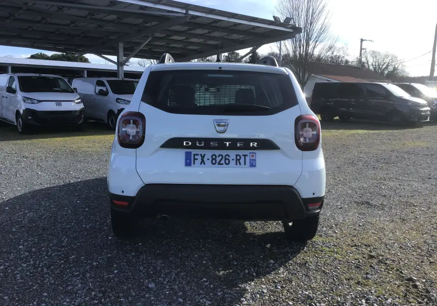 Vue arrière d'un Dacia Duster blanc 2021 avec grille de séparation visible à travers la lunette arrière.