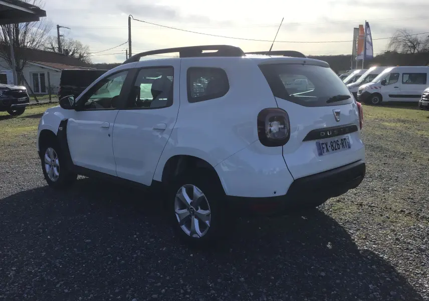 Vue 3/4 arrière droite d'un Dacia Duster blanc 2021 avec jantes alliage et grille de séparation visible à l'arrière.