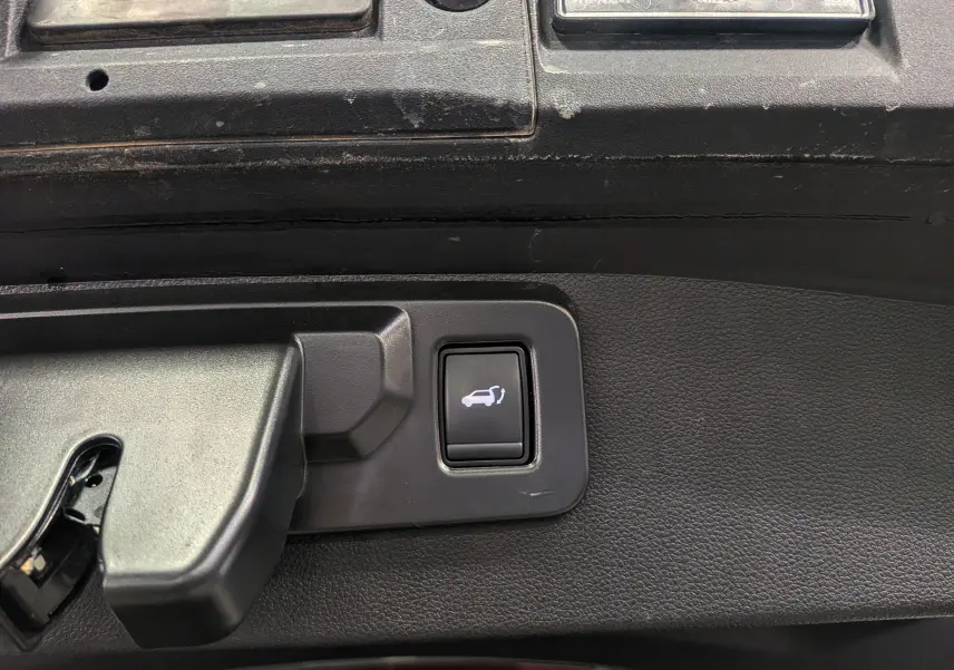 Bouton d'ouverture électrique du coffre sur panneau intérieur noir d'un Renault SYMBIOZ E-TECH gris Cassiopé.