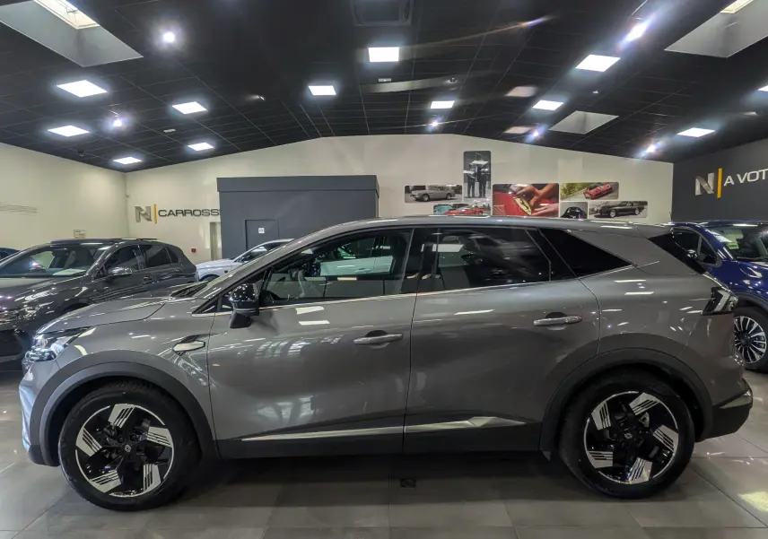 Renault Symbioz E-Tech gris Cassiopé, vue profil côté gauche, jantes noires à motifs géométriques, intérieur visible.