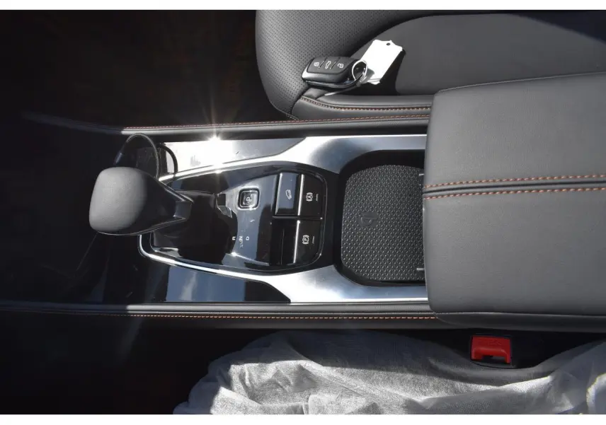 Vue plongeante sur la console centrale noire du MG Motor EHS 1.5 Hybrid+ avec levier de vitesses et clé posée sur accoudoir cuir.