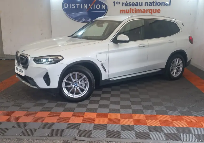 BMW X3 xDrive30e blanc en vue 3/4 avant droit, avec phares LED allumés et jantes alliage visibles.