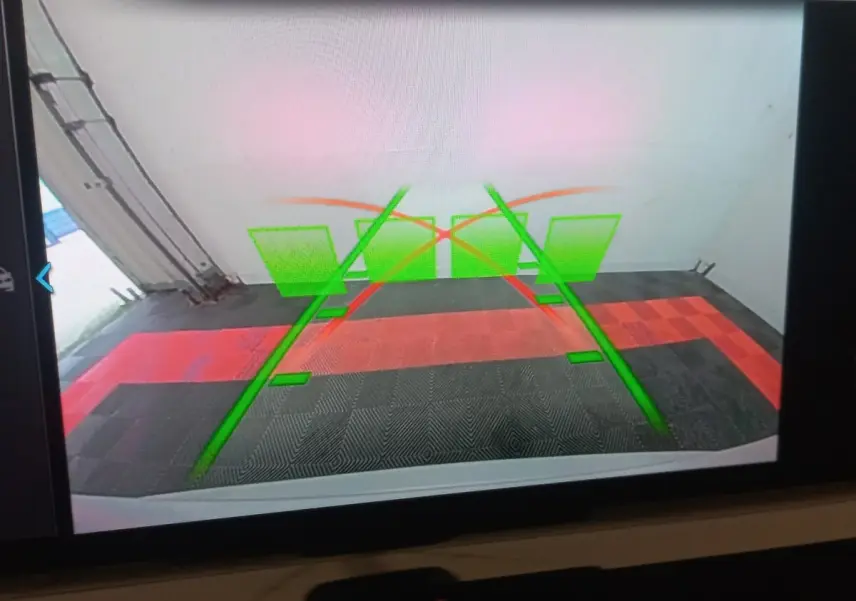 Vue caméra de recul du BMW X3 blanc xDrive30e montrant les lignes de guidage vertes et rouges au sol.