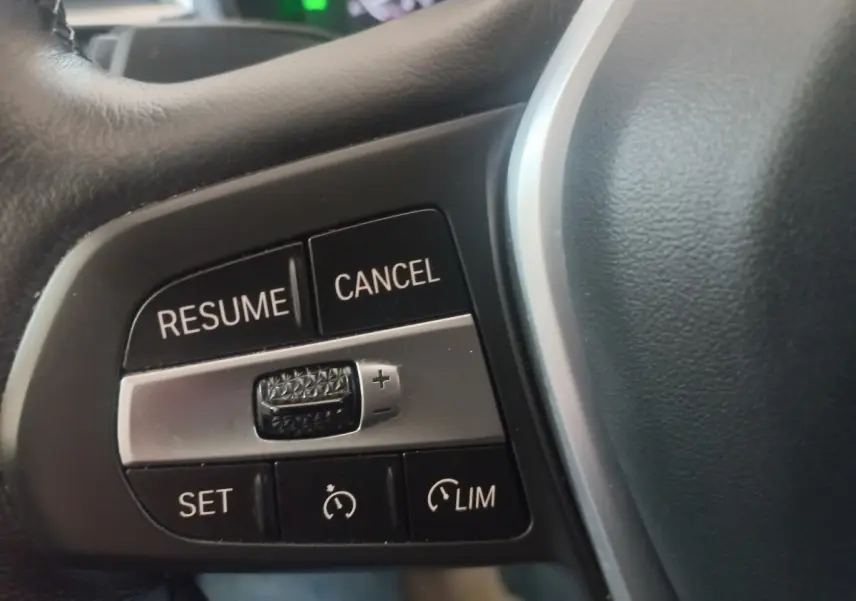 Gros plan sur les commandes du régulateur de vitesse au volant cuir d'une BMW X3 blanc hybride rechargeable.