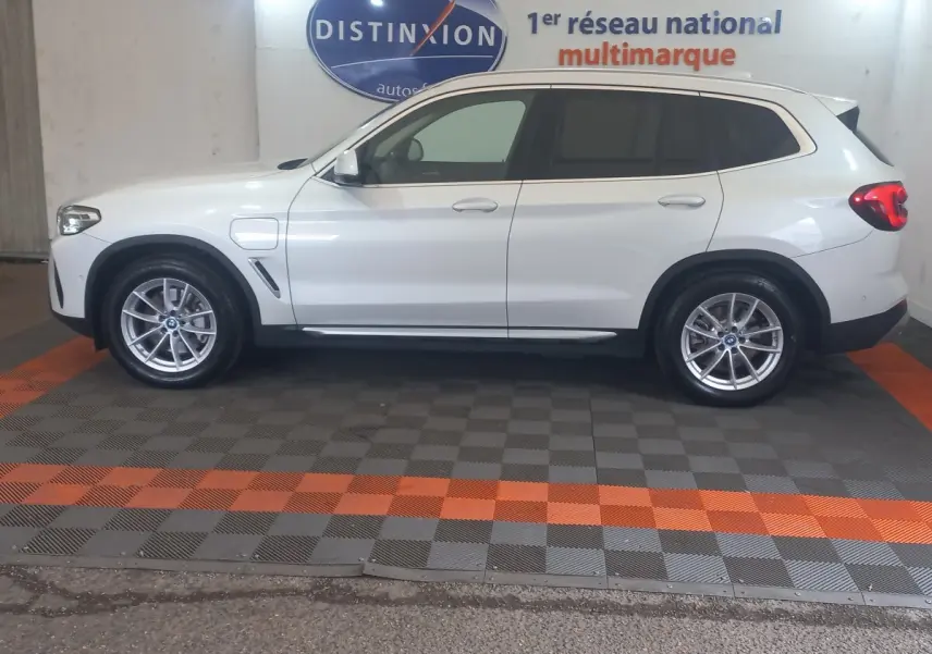 Vue de profil côté gauche d'un BMW X3 xDrive30e blanc, hybride rechargeable, avec jantes alliage et prises de charge visibles.