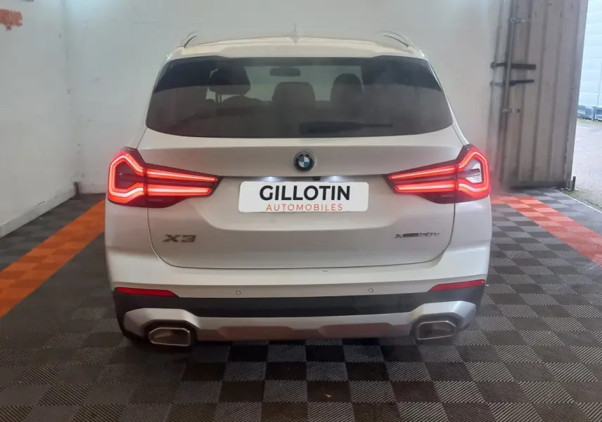 Vue arrière d'un BMW X3 xDrive30e blanc avec feux LED allumés et double sortie d'échappement rectangulaire.