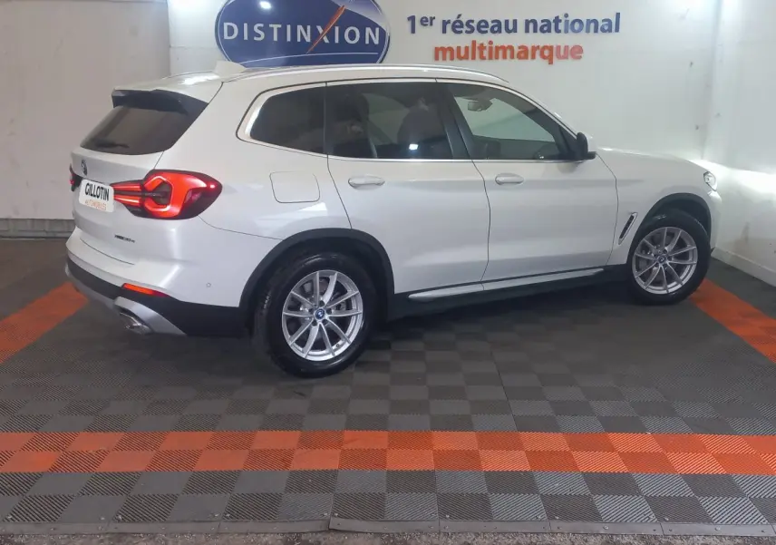 BMW X3 xDrive30e blanc en vue profil droit, avec feux arrière allumés dans un showroom intérieur.