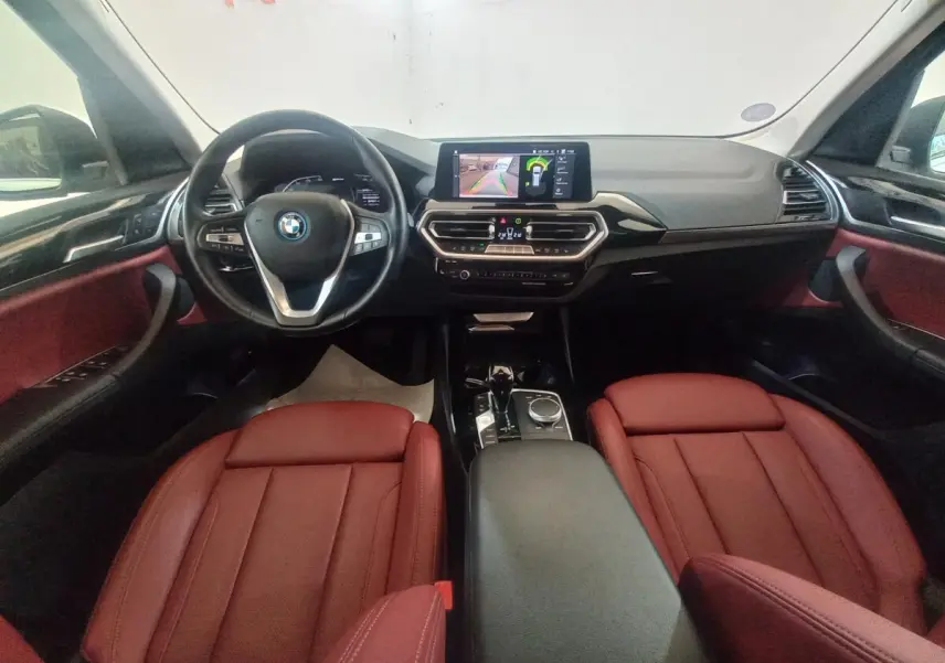 Vue intérieure avant du BMW X3 xDrive30e 2022 avec sièges cuir rouge et tableau de bord noir équipé d’un écran tactile central.