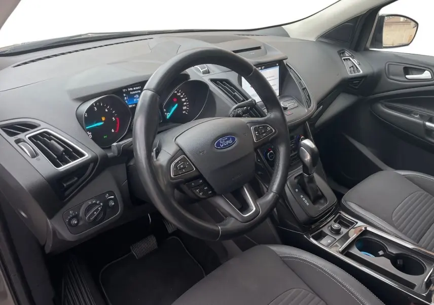 Vue intérieure côté conducteur du Ford Kuga 2017, tableau de bord noir avec volant multifonction et console centrale moderne.