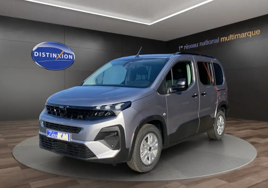 Peugeot Rifter gris clair vu en 3/4 avant droit, avec calandre noire et jantes argentées, en showroom intérieur.