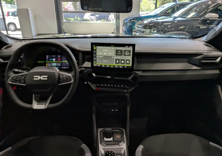 Vue intérieure avant du tableau de bord du Dacia Duster Hybrid-G 150 CH 4x4, avec écran tactile central et volant multifonction.