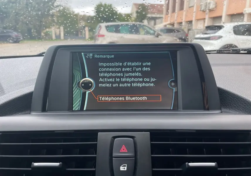 Écran central du tableau de bord de la BMW Série 2 Coupé F22 blanc, affichant un message Bluetooth sous la pluie.
