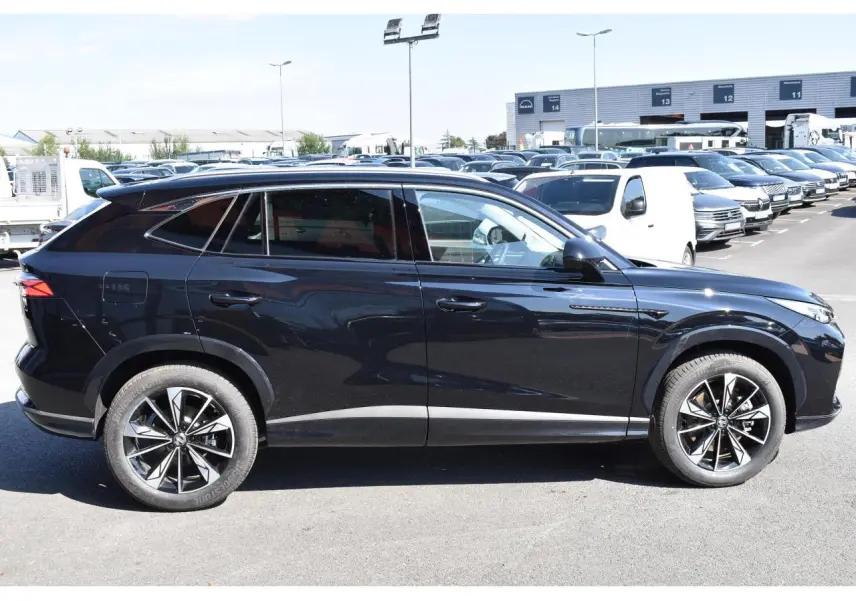 Profil côté gauche du MG Motor EHS 1.5 Hybrid+ noir métallisé avec jantes alliage 19 pouces sur parking.