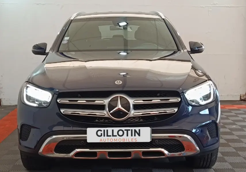 Vue frontale d'un Mercedes GLC 300 DE Business Line hybride rechargeable bleu avec calandre chromée et phares LED allumés.