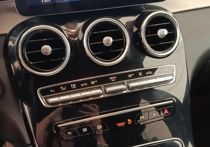 Gros plan sur la console centrale noire brillante du Mercedes GLC 300 hybride, avec aérateurs ronds et commandes climatisation.