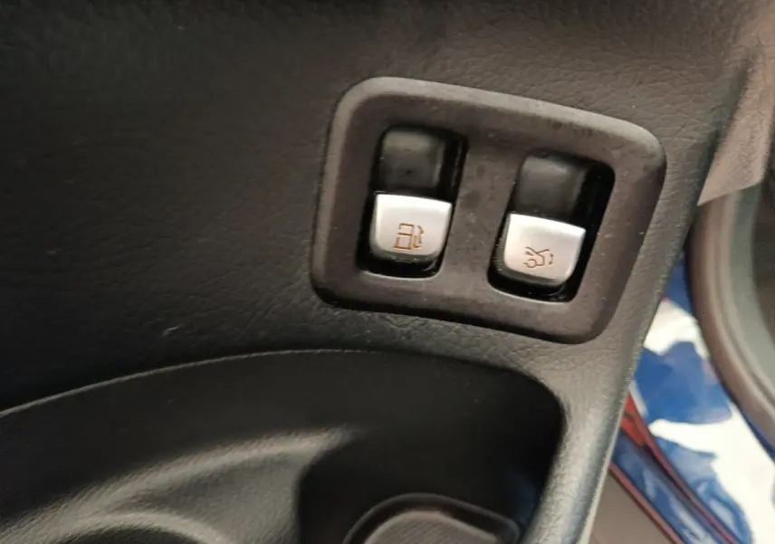 Gros plan sur les boutons d’ouverture de trappe à carburant et coffre dans l’habitacle d’un Mercedes GLC bleu.