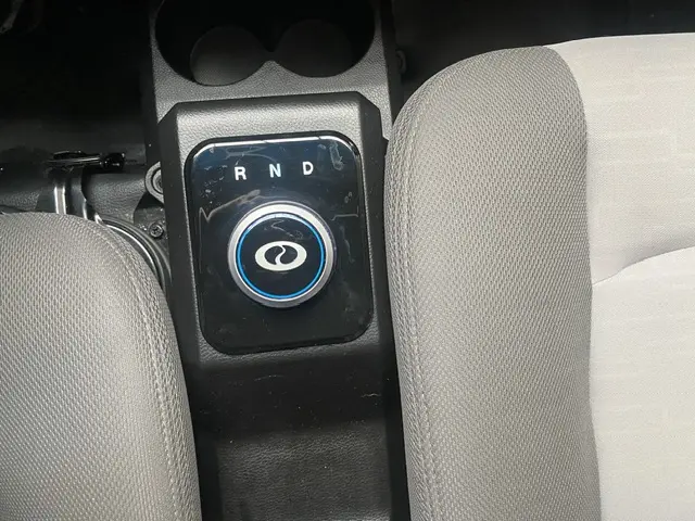 Gros plan sur la molette de boîte automatique noire avec logo DFSK entre les sièges gris clair du DFSK EC35 blanc électrique.