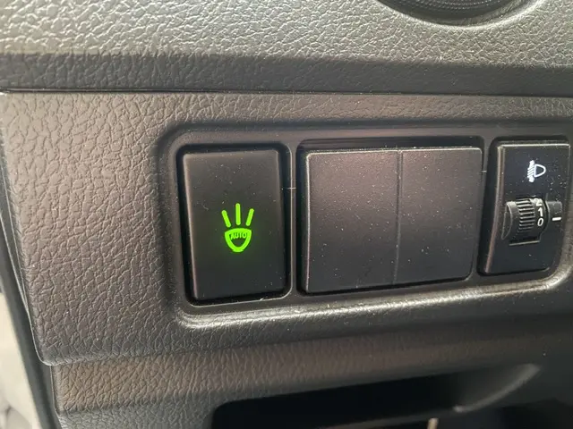 Gros plan sur le tableau de bord noir du DFSK EC35 blanc, bouton vert d'allumage automatique des phares visible à gauche.