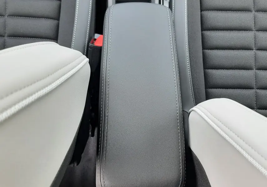 Vue plongeante sur l'accoudoir central noir entre les sièges avant gris clair et tissu noir du Citroën C3 Aircross 2026.