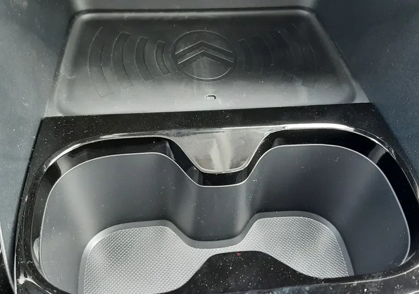 Gros plan intérieur sur le porte-gobelets noir brillant et le chargeur sans fil avec logo Citroën du Citroën C3 Aircross blanc banquise.