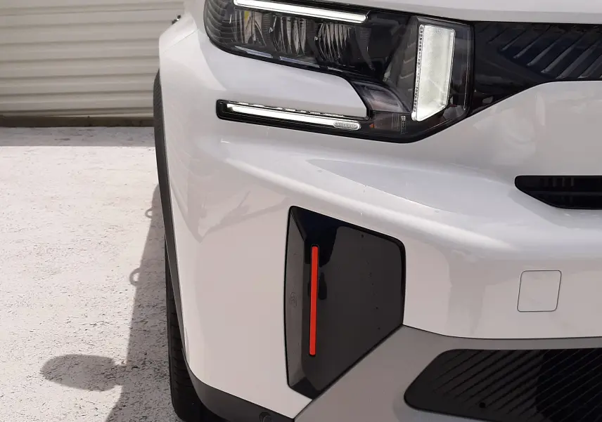 Gros plan sur l'avant gauche du Citroën C3 Aircross blanc banquise avec toit noir, mettant en valeur le phare LED et le détail rouge du pare-chocs.