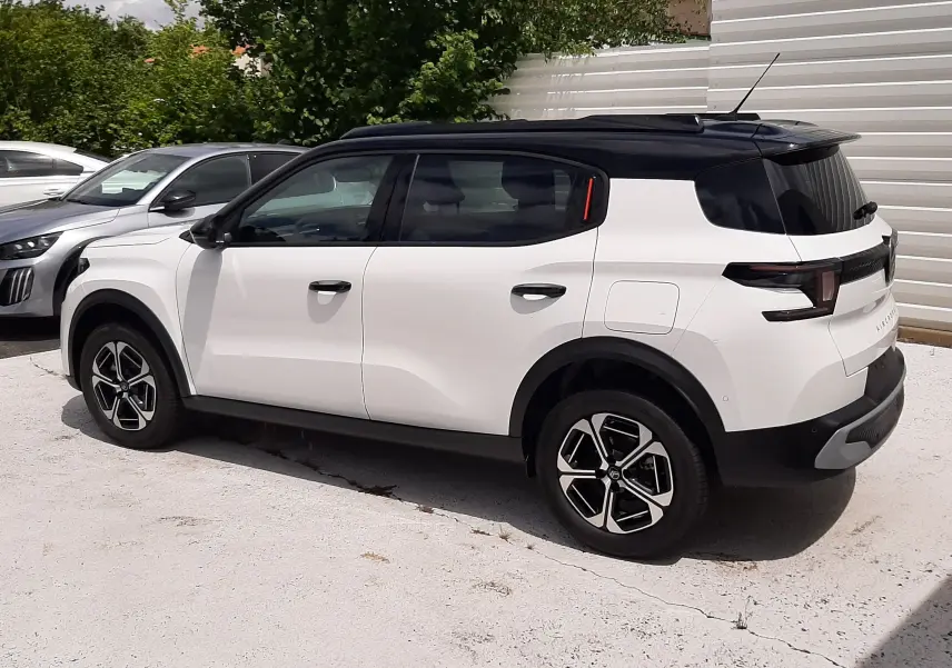 Vue côté droit arrière d'un Citroën C3 Aircross blanc banquise avec toit noir, roues alliage et vitres teintées.