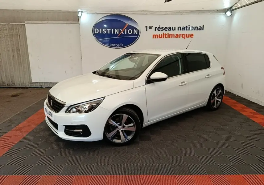 Peugeot 308 blanc vue 3/4 avant droit dans un showroom avec jantes alliage et phares allumés.