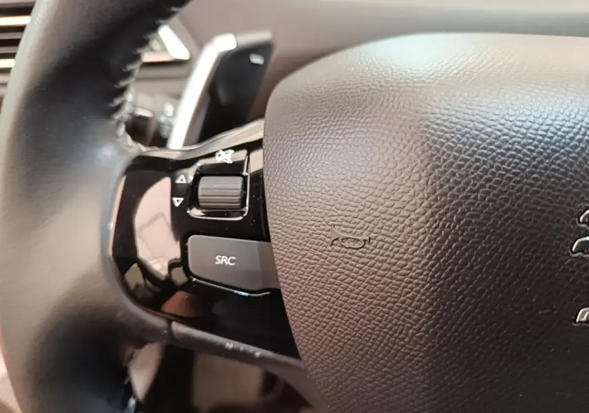 Gros plan sur le volant cuir noir de la Peugeot 308 2020, avec commandes audio intégrées côté gauche.