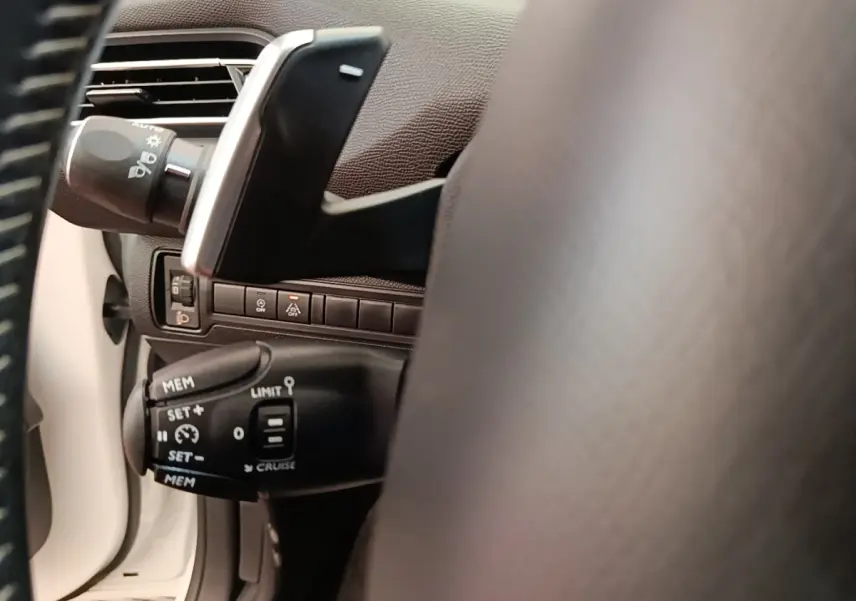Gros plan sur la commande de régulateur de vitesse à gauche du volant dans l’habitacle blanc du Peugeot 308 2020.