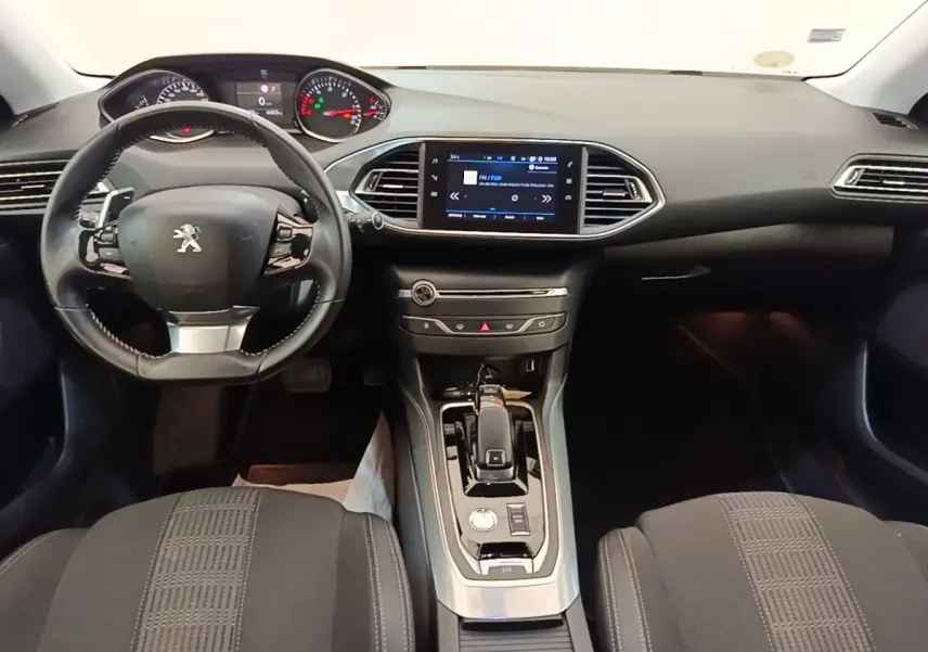 Vue intérieure avant de la Peugeot 308 blanche, tableau de bord avec écran tactile et volant cuir multifonctions.