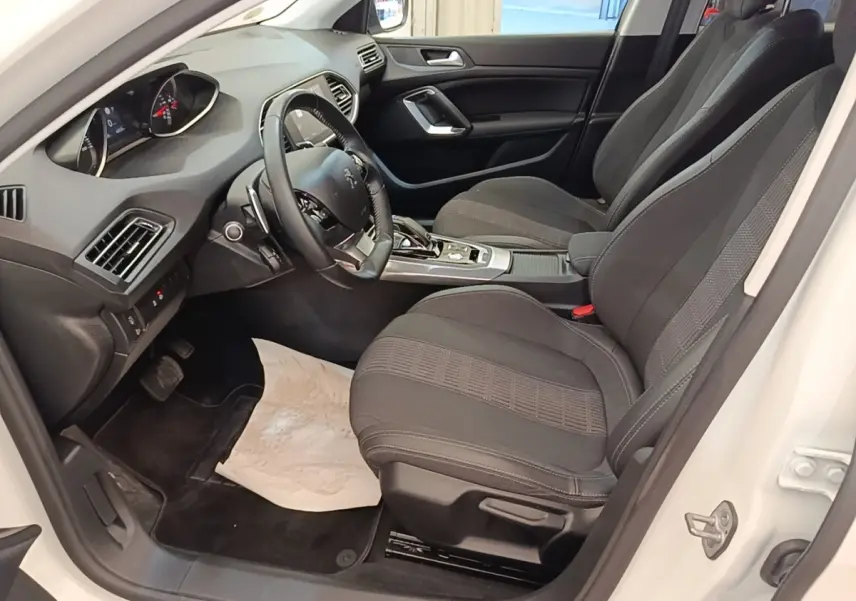 Intérieur avant droit d’une Peugeot 308 blanche, sièges noirs, volant cuir multifonctions et tableau de bord moderne.