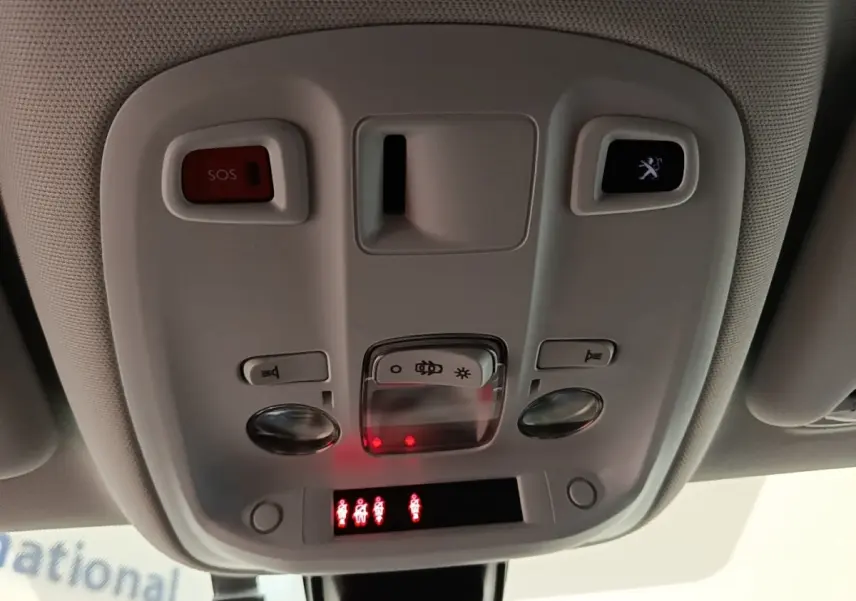 Vue intérieure en gros plan du plafonnier de la Peugeot 308 blanc, avec boutons SOS et éclairage, et témoins rouges allumés.