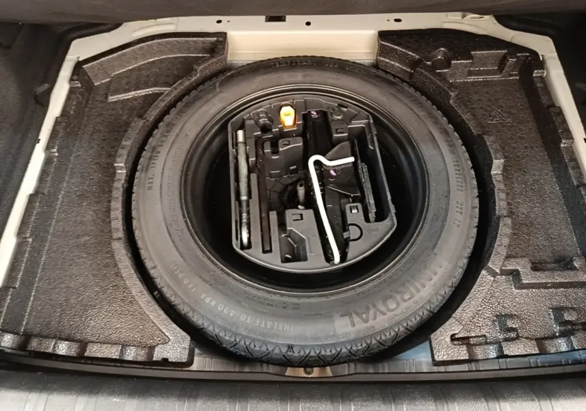 Vue plongeante sur la roue de secours et les outils de bord dans le coffre d'une Peugeot 308 blanche.