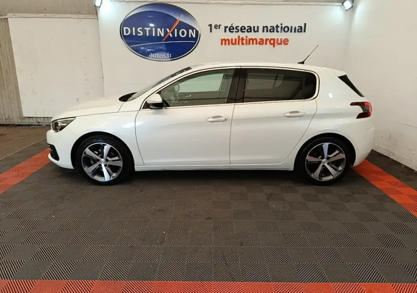 Profil latéral droit d'une Peugeot 308 blanche 2020 dans un showroom avec sol gris et rouge.