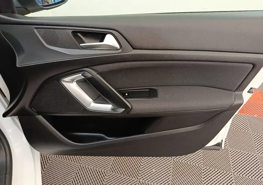 Vue intérieure côté gauche de la porte avant blanche de la Peugeot 308 avec poignée argentée et garniture noire.