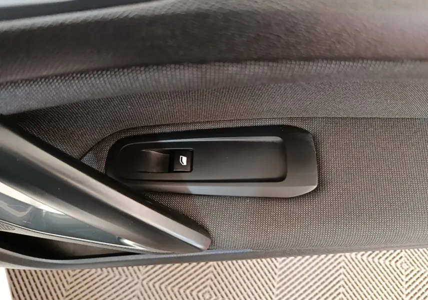 Détail de la commande de lève-vitre électrique sur la porte intérieure côté gauche d’une Peugeot 308 blanche.