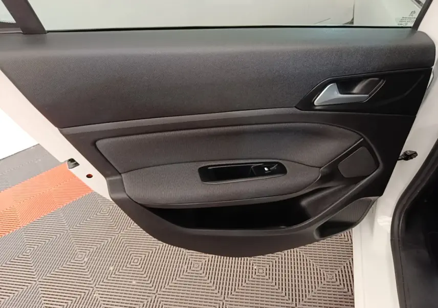 Vue intérieure de la porte avant gauche d'une Peugeot 308 blanche, avec garniture noire et commande de vitre électrique.