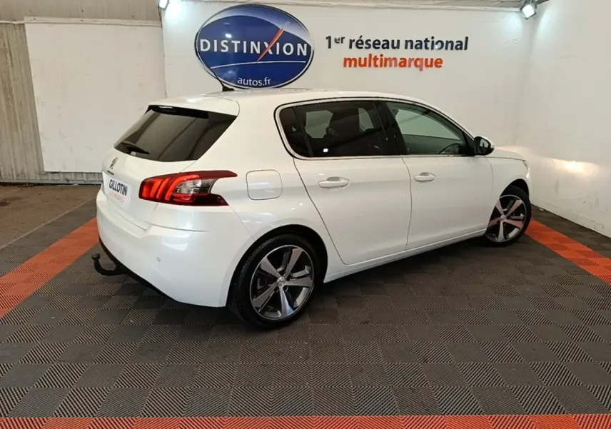Vue 3/4 arrière droite d'une Peugeot 308 blanche en intérieur, avec jantes alliage et feux arrière LED distinctifs.