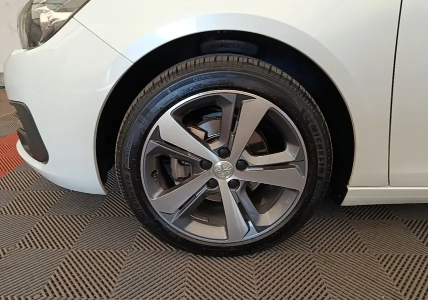 Gros plan sur la roue avant gauche de la Peugeot 308 blanche, mettant en valeur la jante alliage moderne.