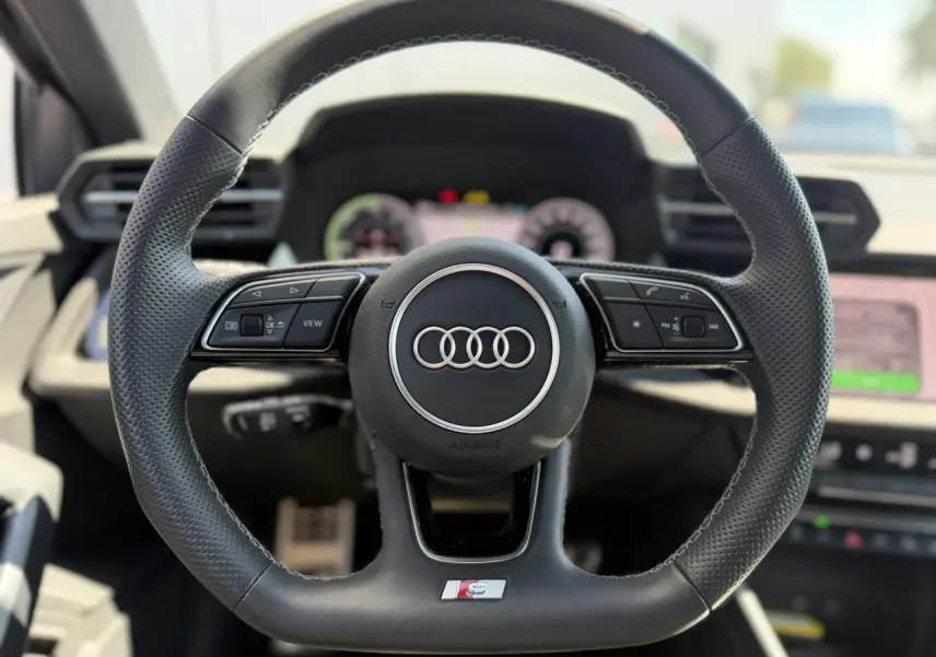 Volant sport en cuir perforé avec logo S Audi, vue frontale centrée sur le tableau de bord intérieur noir.