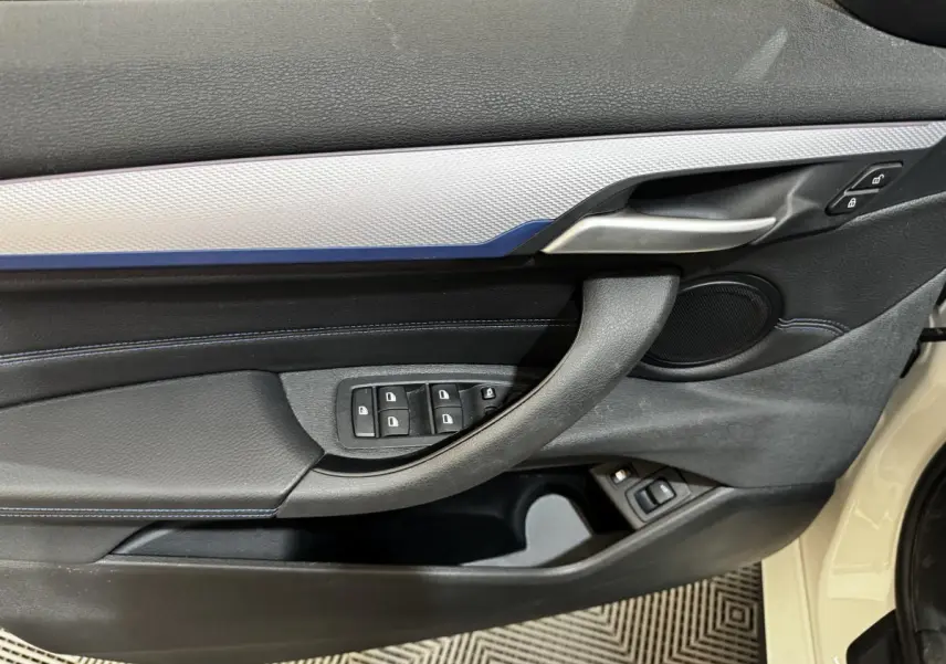 Détail de la porte avant gauche d’une BMW X2 blanche 2022, avec commandes des vitres et poignée alu.
