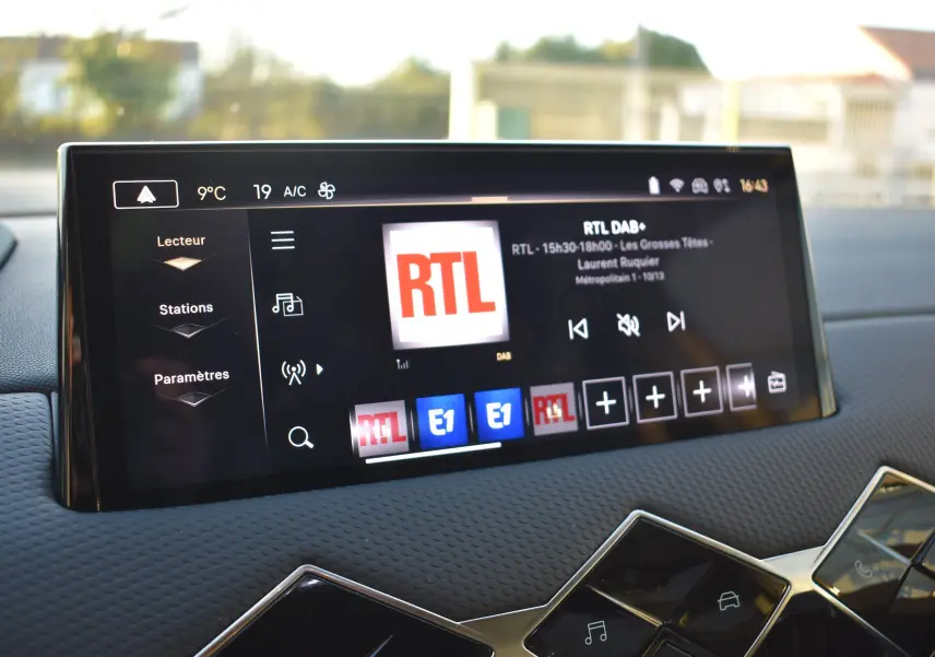 Écran tactile central du DS3 Crossback 2024 affichant la radio RTL, avec tableau de bord noir texturé en arrière-plan.