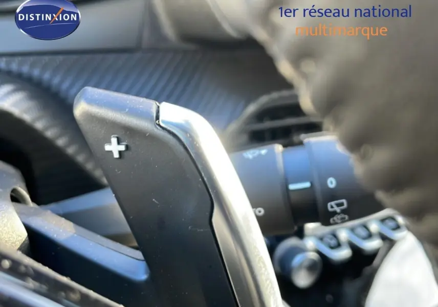 Gros plan sur la palette de changement de vitesse + au volant d’une Peugeot 208 noire, intérieur gris noir.