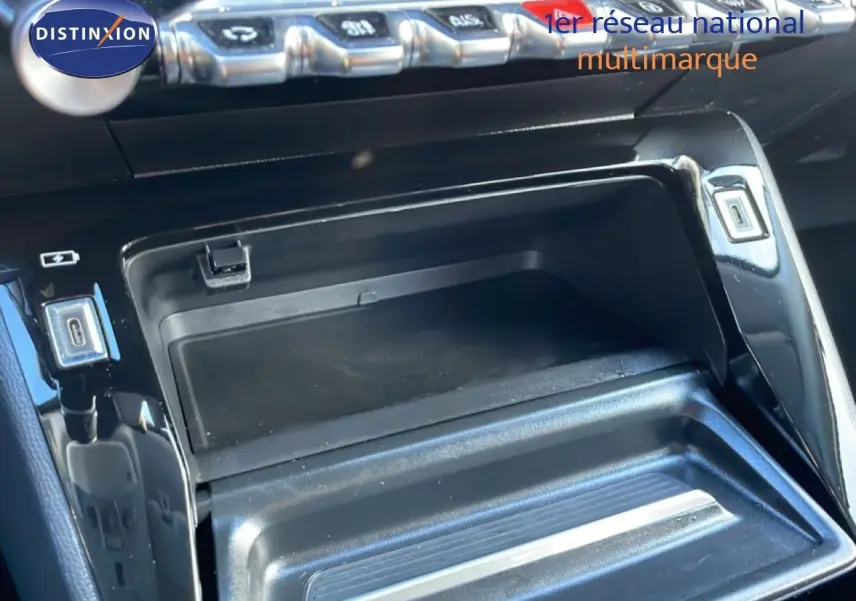 Vue rapprochée de la console centrale noire de la Peugeot 208 1.2 Hybrid 110ch, avec compartiment ouvert et boutons argentés.