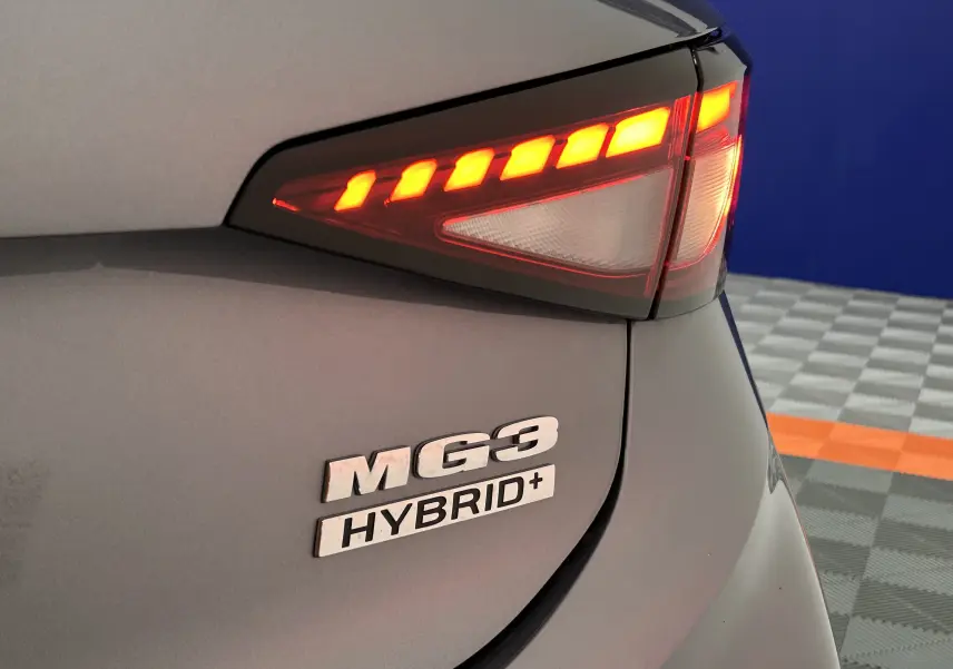 Gros plan sur le feu arrière droit allumé et le logo MG3 Hybrid+ sur la carrosserie grise Hampstead.